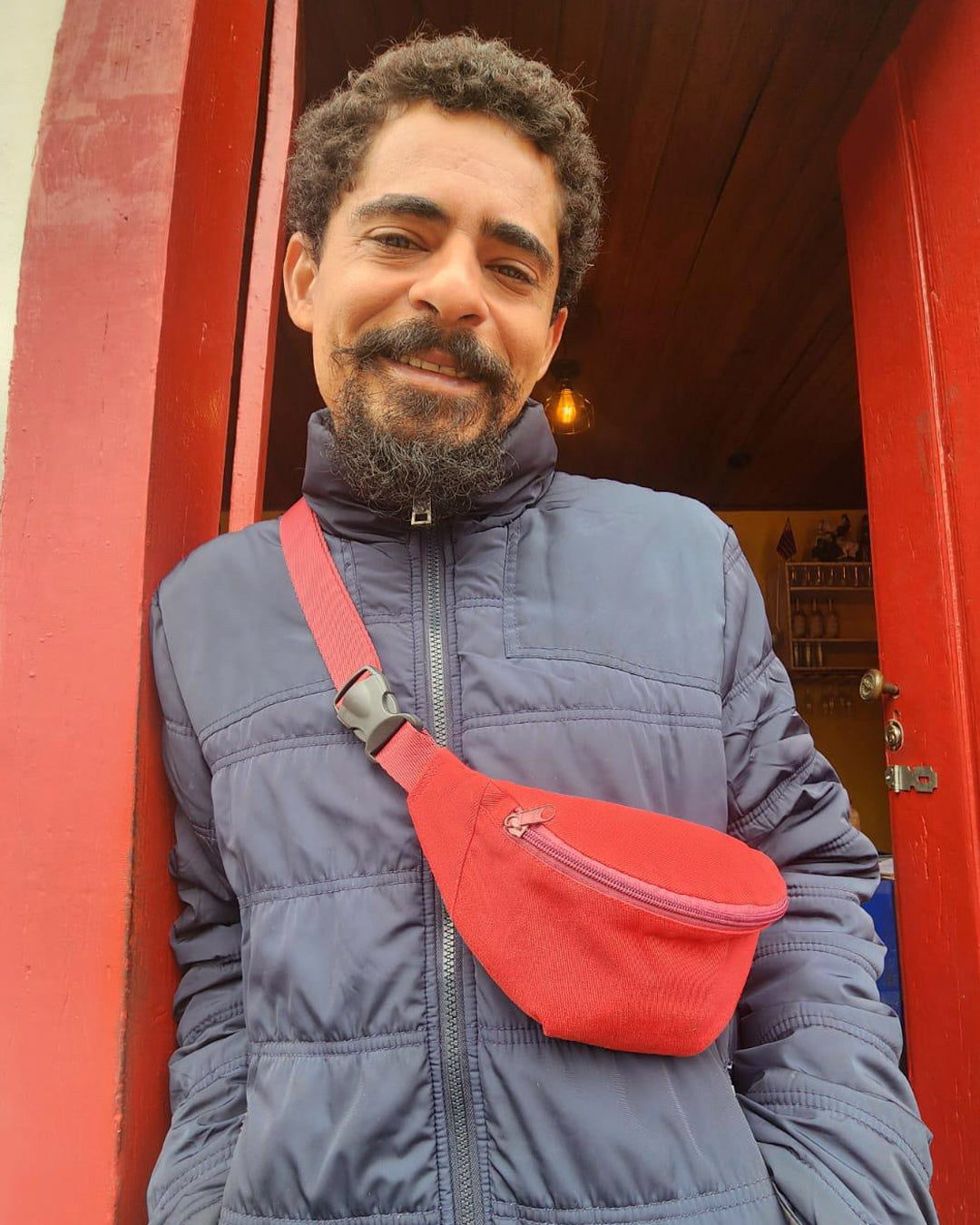 Pessoa usando pochete CerejaTá Mara atravessada, na frente de um bar.